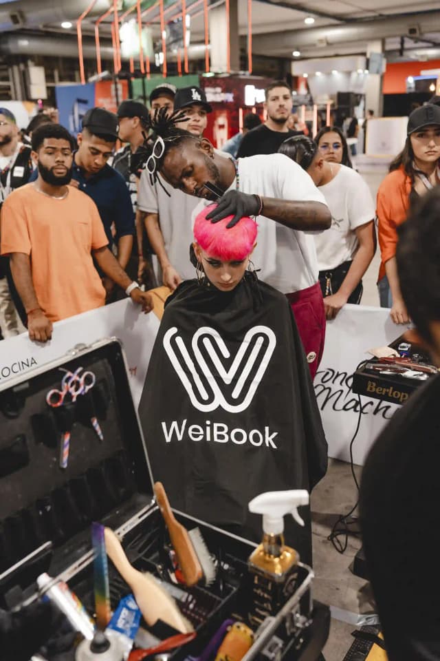 Estilista aplicando color rosa durante demostración en vivo con capa de Weibook